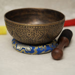 Handmade Tibetan singing bowl with flower, leaf, and vine mandala carvings,  used for meditation and sound healing.