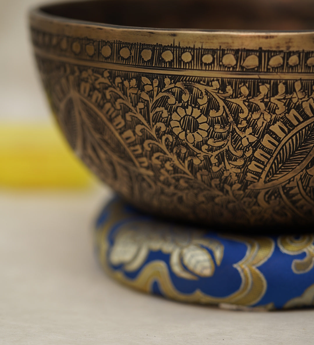 Handmade Tibetan singing bowl with flower, leaf, and vine mandala carvings,  used for meditation and sound healing.