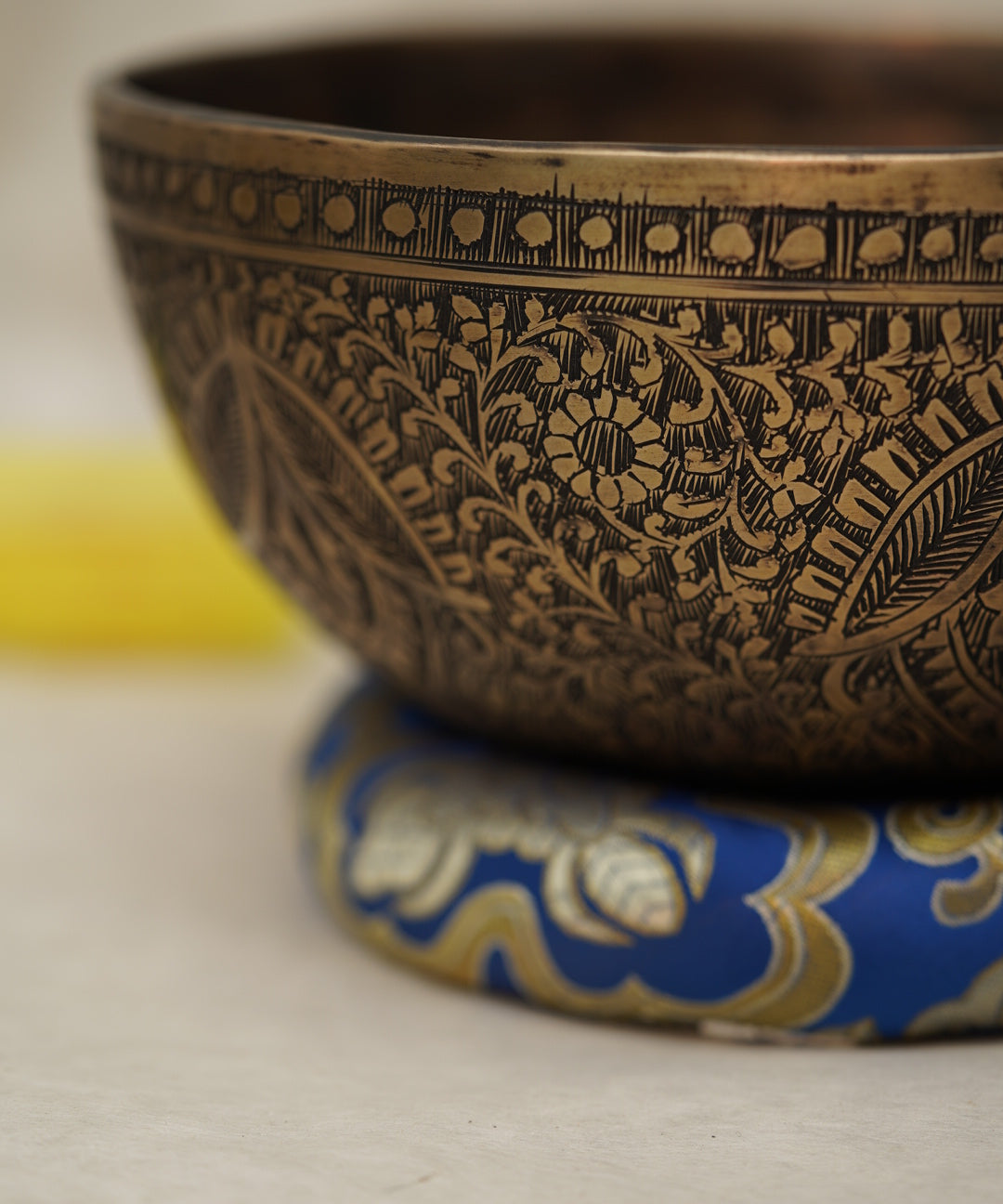 Handmade Tibetan singing bowl with flower, leaf, and vine mandala carvings,  used for meditation and sound healing.