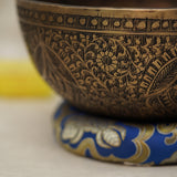 Handmade Tibetan singing bowl with flower, leaf, and vine mandala carvings,  used for meditation and sound healing.