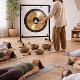 Person striking a handmade gong in a yoga studio with people lying on mats.