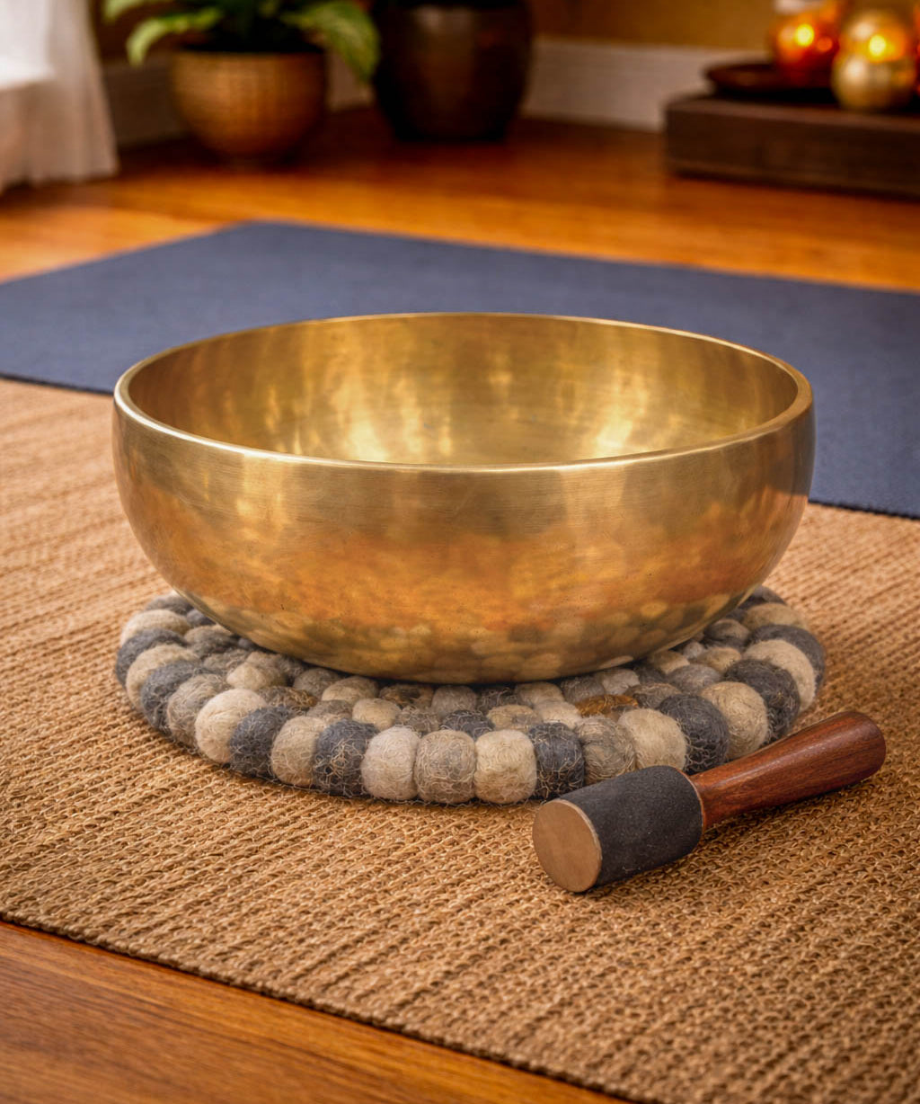 Brass singing bowl with a wooden handle on a textured mat in a room setting.