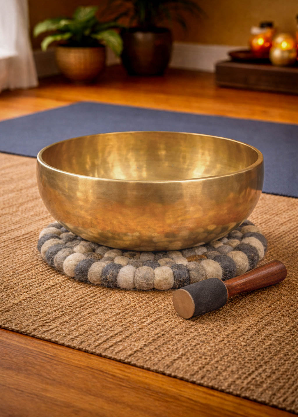 Brass singing bowl with a wooden handle on a textured mat in a room setting.
