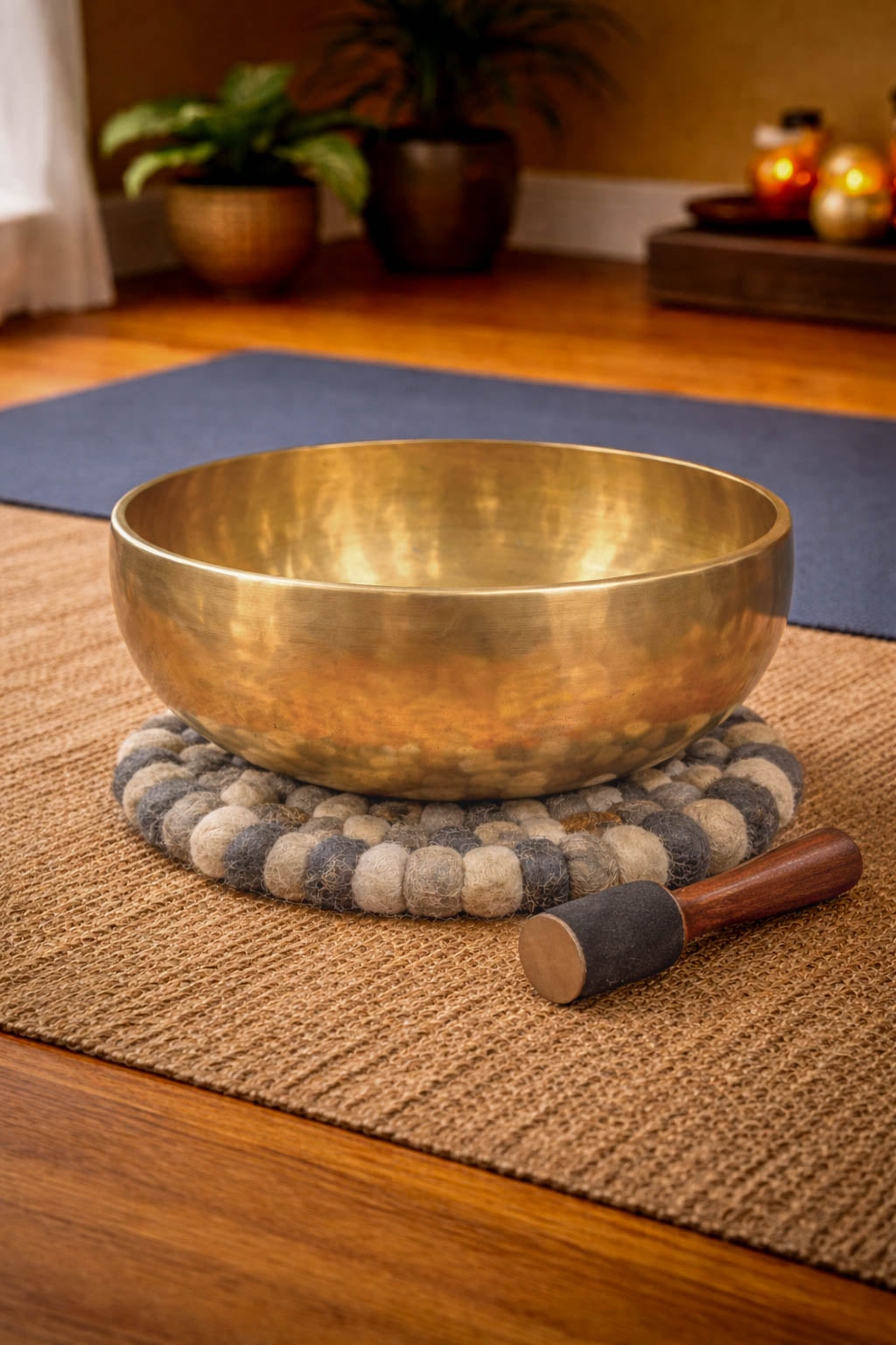 Brass singing bowl with a wooden handle on a textured mat in a room setting.