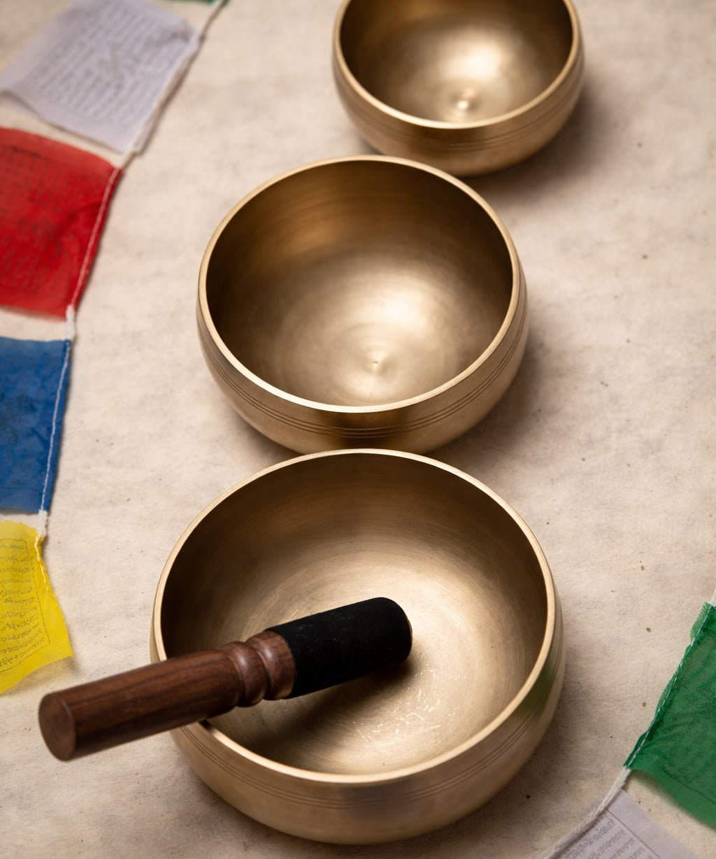 Three brass singing bowls on a textured surface with prayer flags in the background