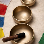Three brass singing bowls on a textured surface with prayer flags in the background