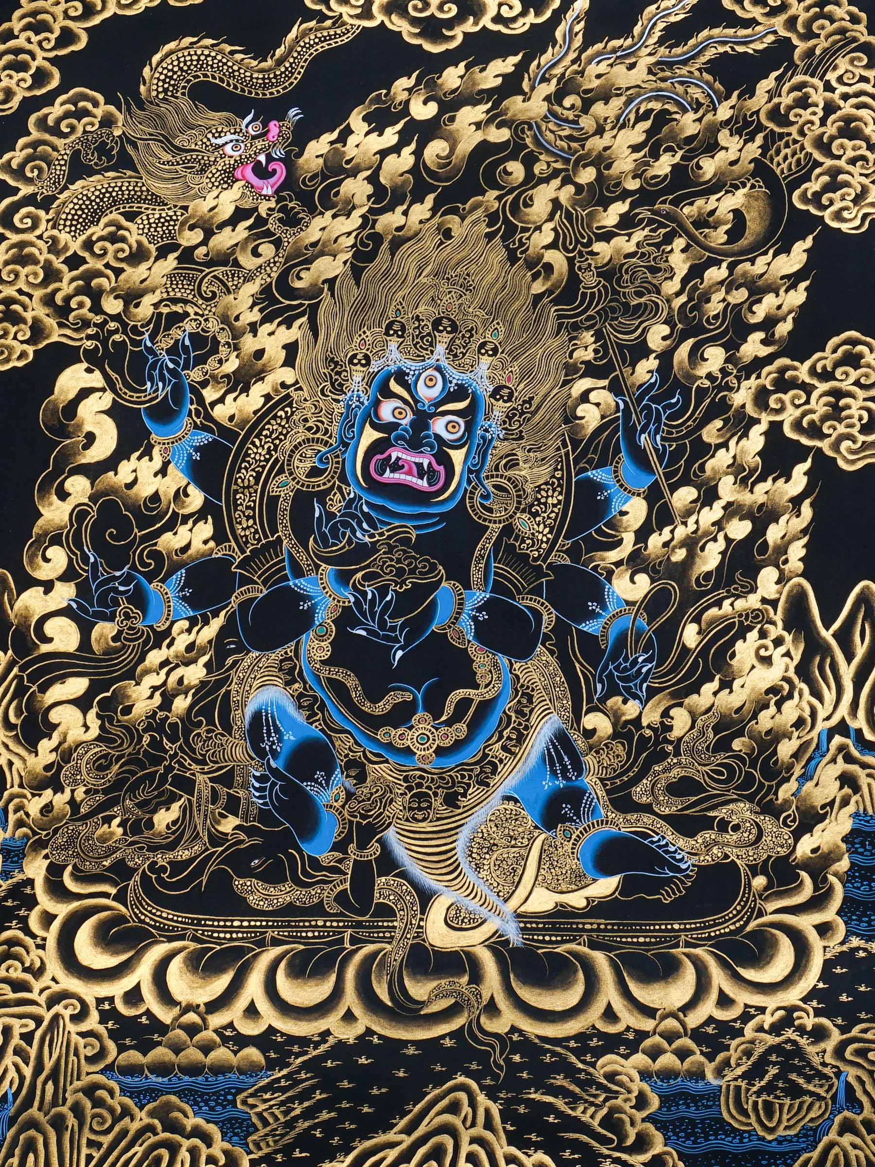 Mahakala thangka painting showing a wrathful blue Mahakala deity with multiple arms, flaming aura, gold clouds, dragon motif, and black background in traditional Tibetan Buddhist style.