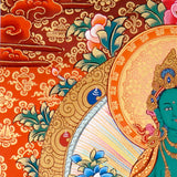 Green Tara Thangka Painting showing the Tibetan Buddhist goddess seated on a pink lotus throne with one leg extended, holding a lotus flower, surrounded by a radiant halo, sacred ornaments and red-gold background.
