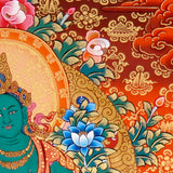 Green Tara Thangka Painting showing the Tibetan Buddhist goddess seated on a pink lotus throne with one leg extended, holding a lotus flower, surrounded by a radiant halo, sacred ornaments and red-gold background.