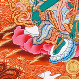 Green Tara Thangka Painting showing the Tibetan Buddhist goddess seated on a pink lotus throne with one leg extended, holding a lotus flower, surrounded by a radiant halo, sacred ornaments and red-gold background.